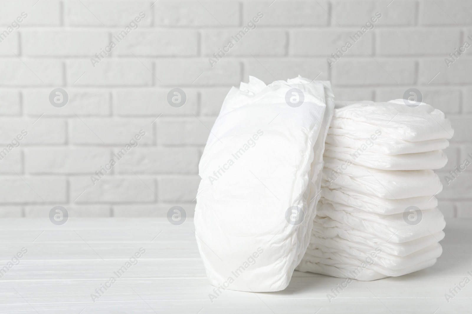 Photo of Baby diapers on wooden table against white brick wall. Space for text