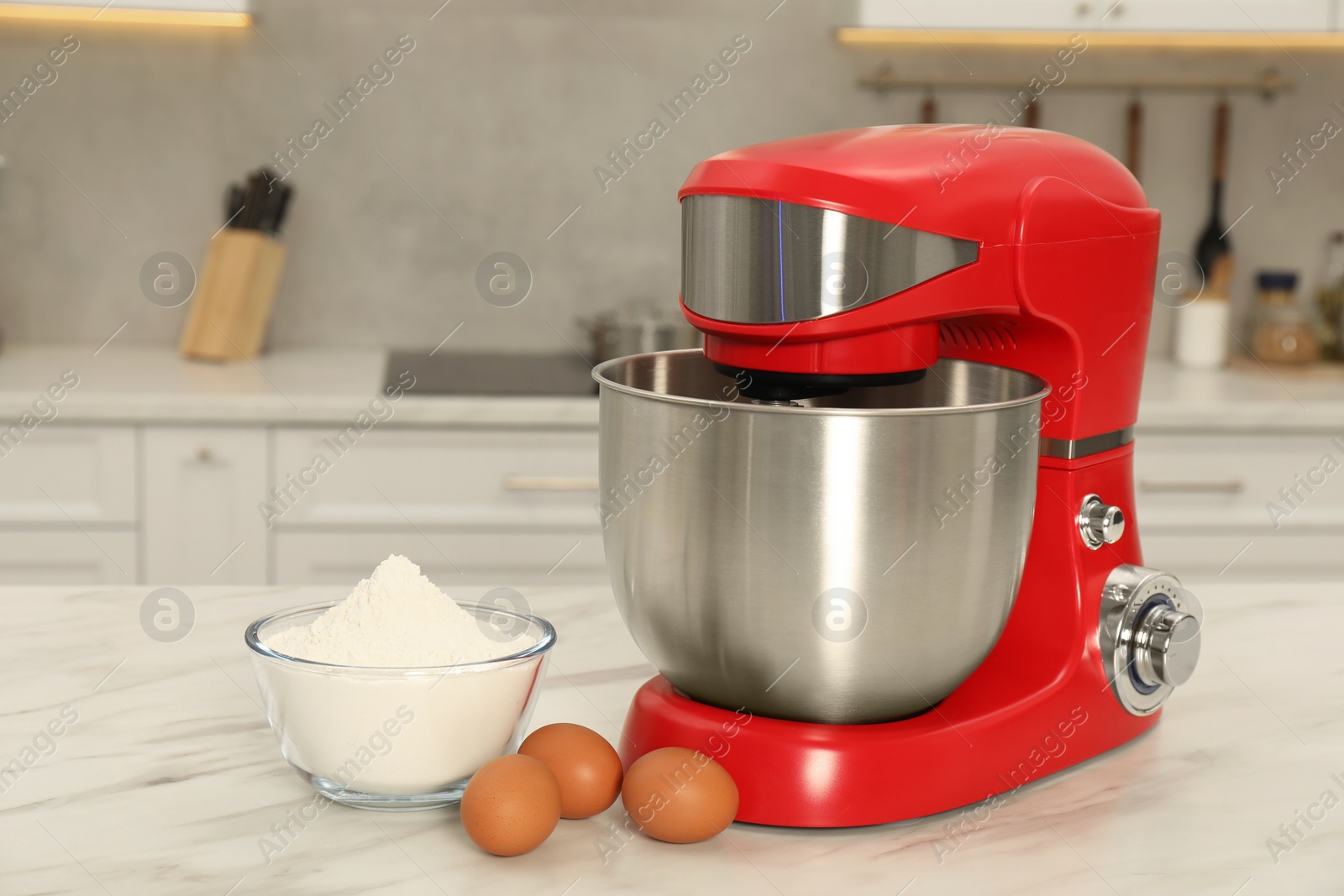 Photo of Modern red stand mixer, eggs and bowl with flour on white marble table in kitchen