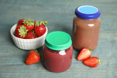 Photo of Jars with baby food and fresh strawberries on light blue wooden table