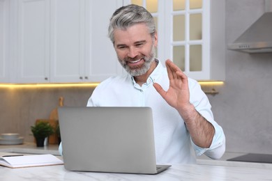 Photo of Man waving hello during video chat via laptop at home