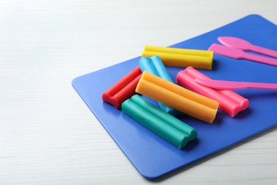 Photo of Many different colorful plasticine pieces with tools on white wooden table