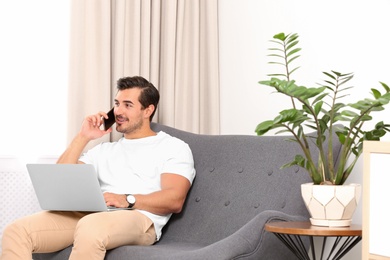Photo of Handsome young man talking on phone while working with laptop indoors