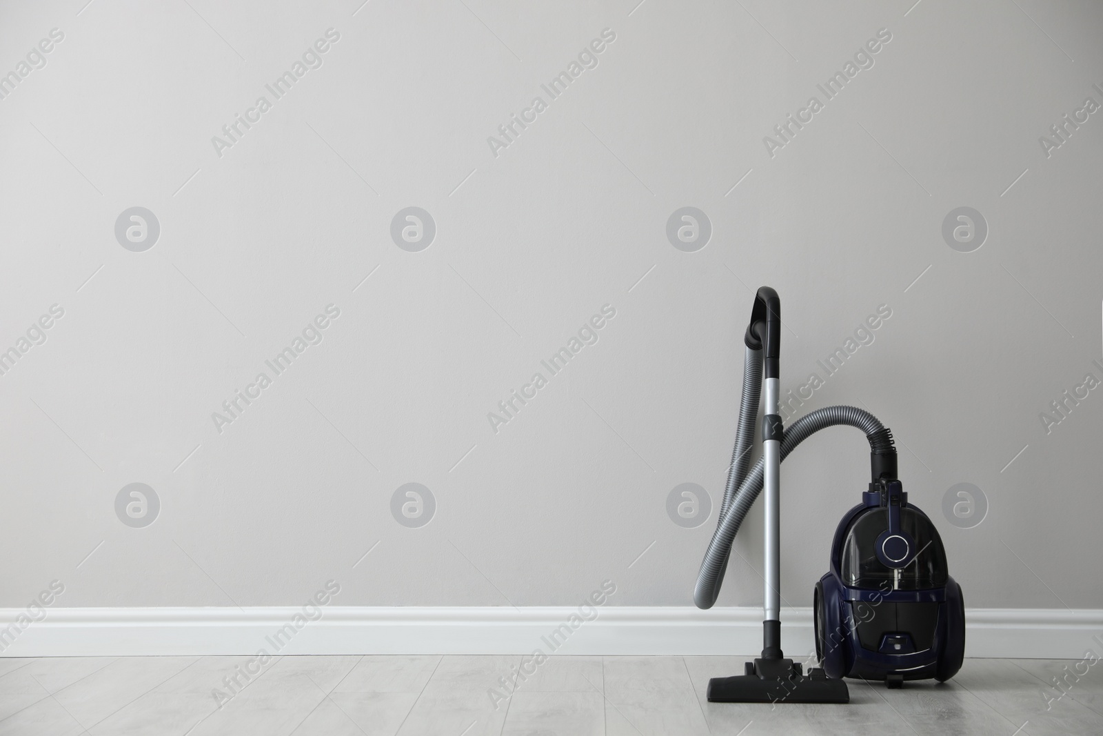 Photo of Modern vacuum cleaner near white wall indoors, space for text