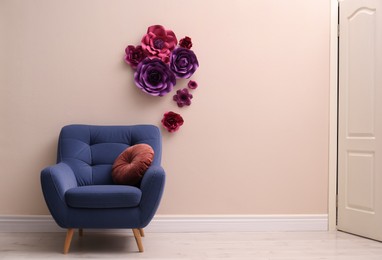 Comfortable armchair near wall with floral decor in room, space for text. Interior design