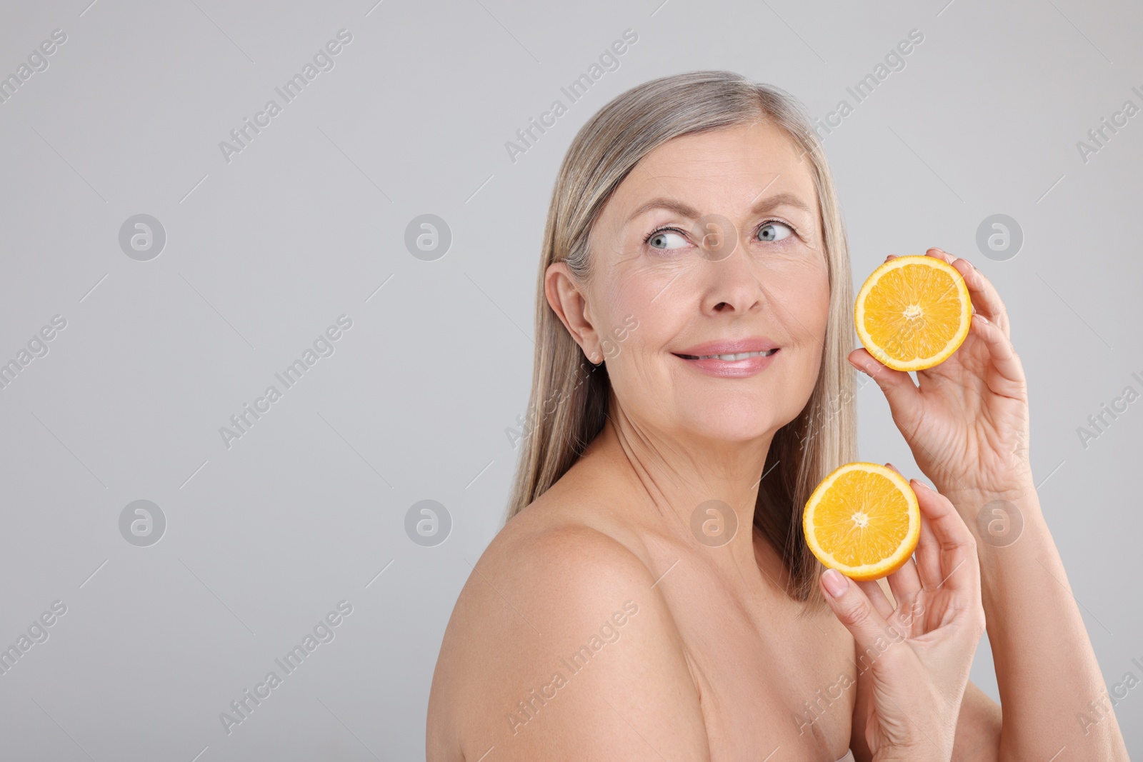 Photo of Beautiful woman with halves of orange rich in vitamin C on grey background, space for text