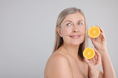 Photo of Beautiful woman with halves of orange rich in vitamin C on grey background, space for text