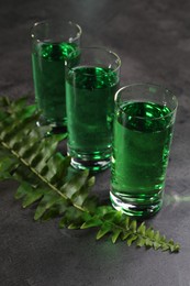 Photo of Absinthe in shot glasses and fern leaf on gray table, closeup. Alcoholic drink