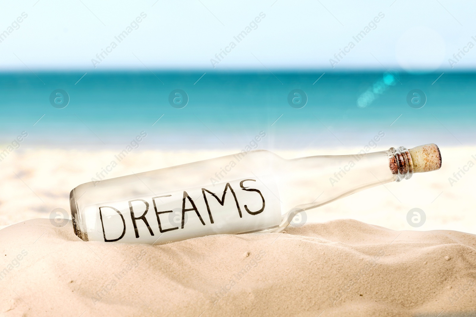 Image of Corked glass bottle with Dreams note on sandy near sea