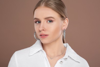 Photo of Beautiful young woman with elegant jewelry on light brown background