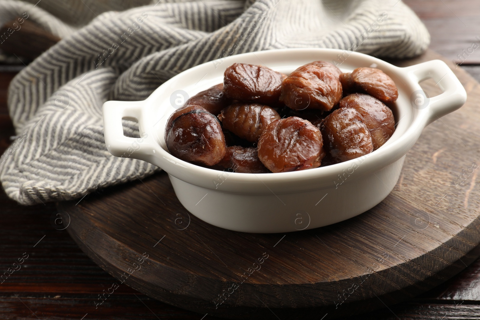 Photo of Roasted edible sweet chestnuts in dish on light wooden table