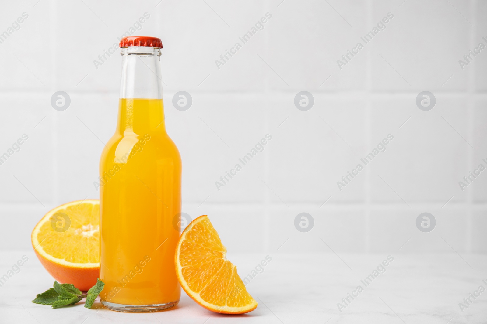 Photo of Delicious kombucha in glass bottle, orange and mint on white table