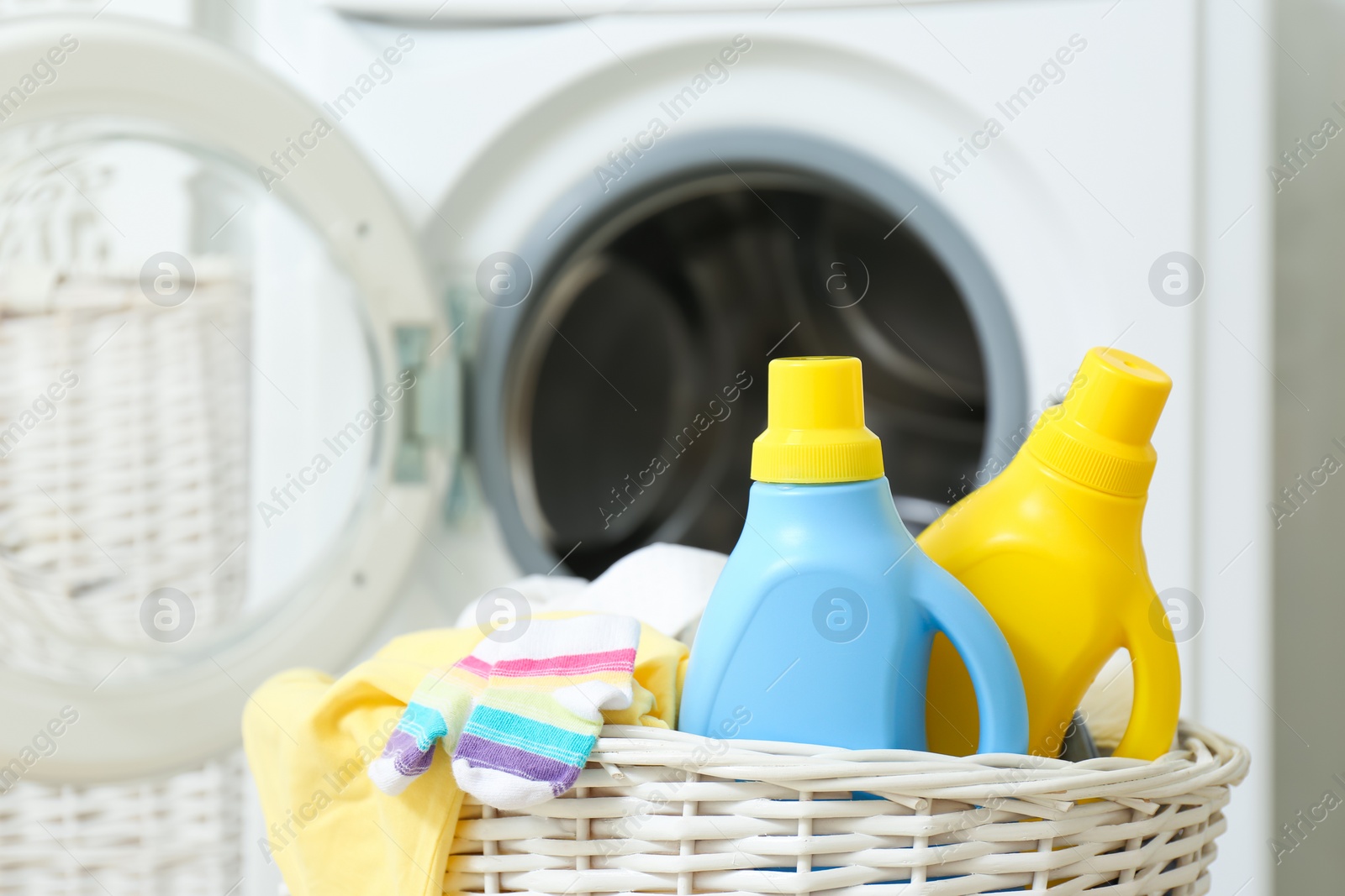 Photo of Bottles of detergent and children's clothes in wicker basket near washing machine indoors