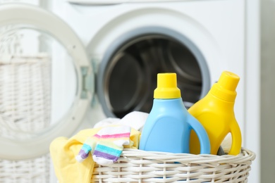 Photo of Bottles of detergent and children's clothes in wicker basket near washing machine indoors