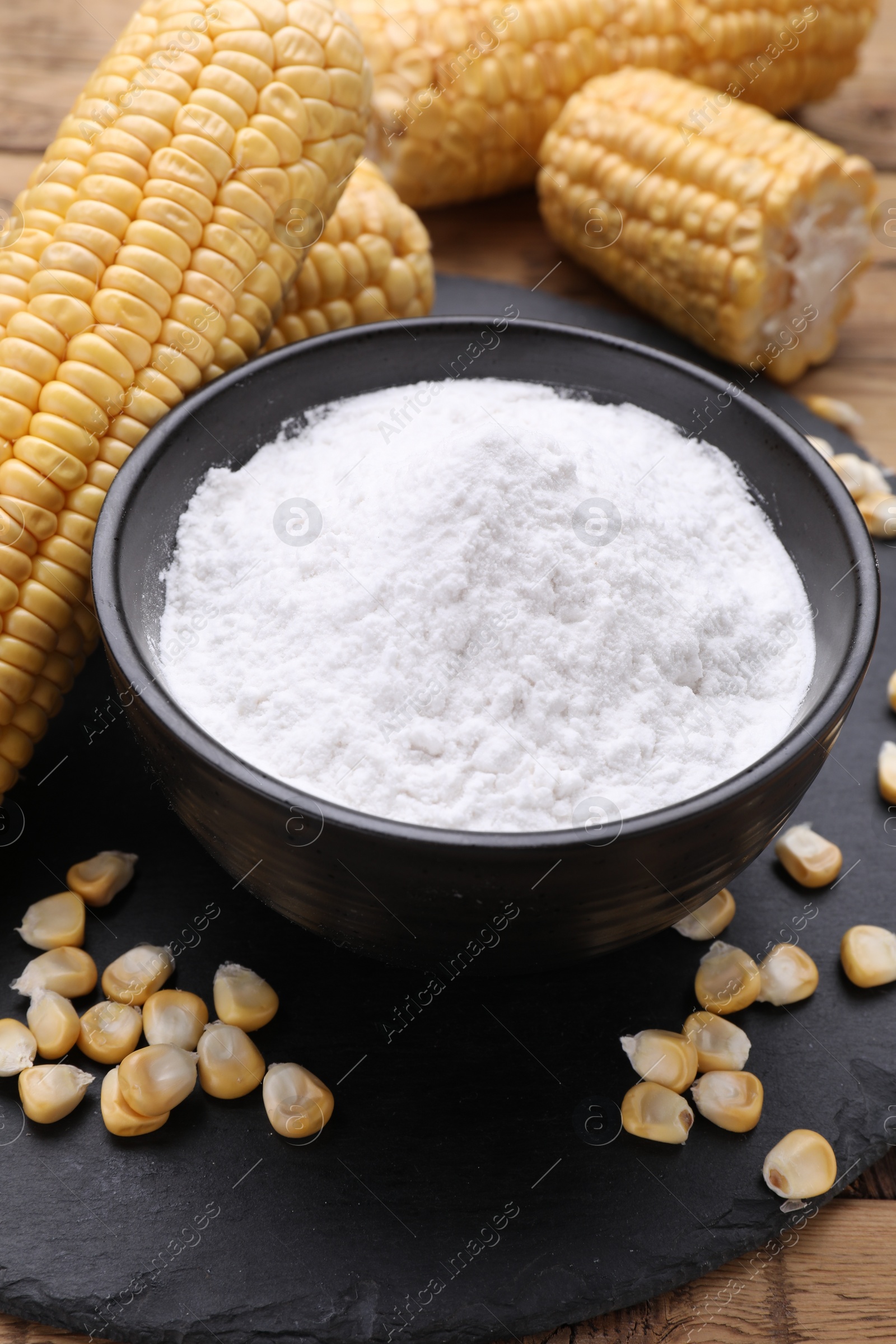 Photo of Bowl with corn starch, ripe cobs and kernels on table, closeup