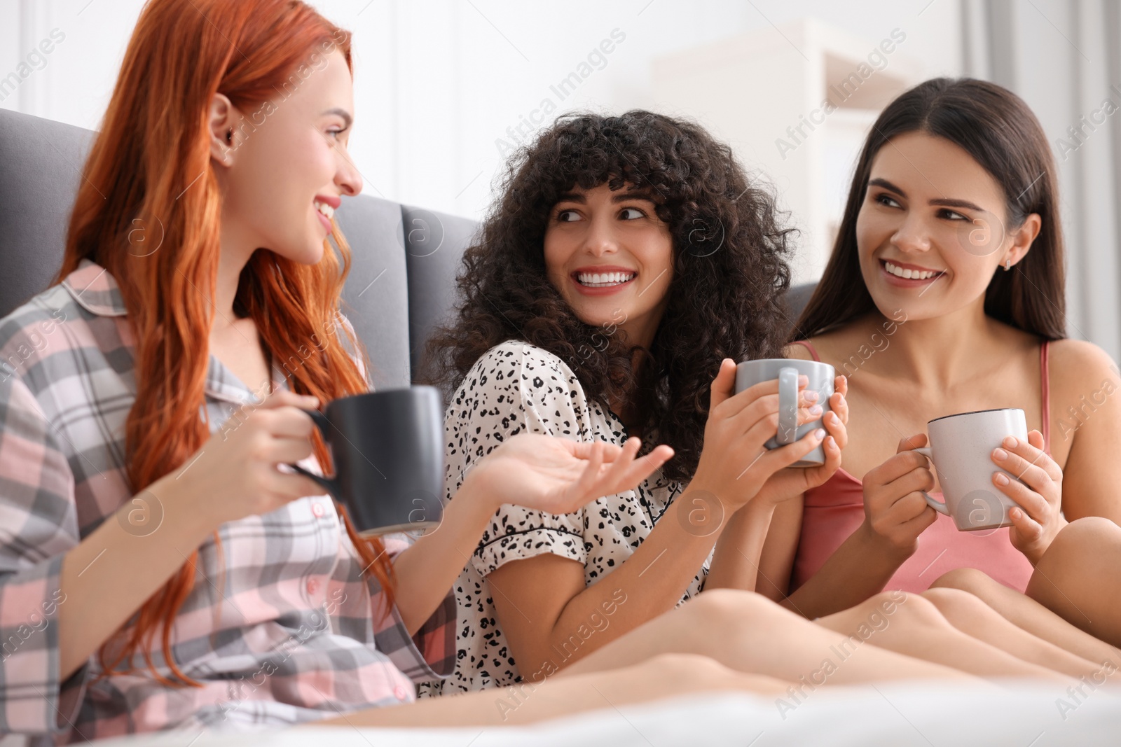 Photo of Happy young friends with cups of drink on bed at home