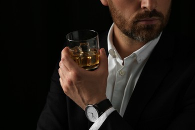 Photo of Man holding glass of whiskey with ice cubes on black background, closeup. Space for text