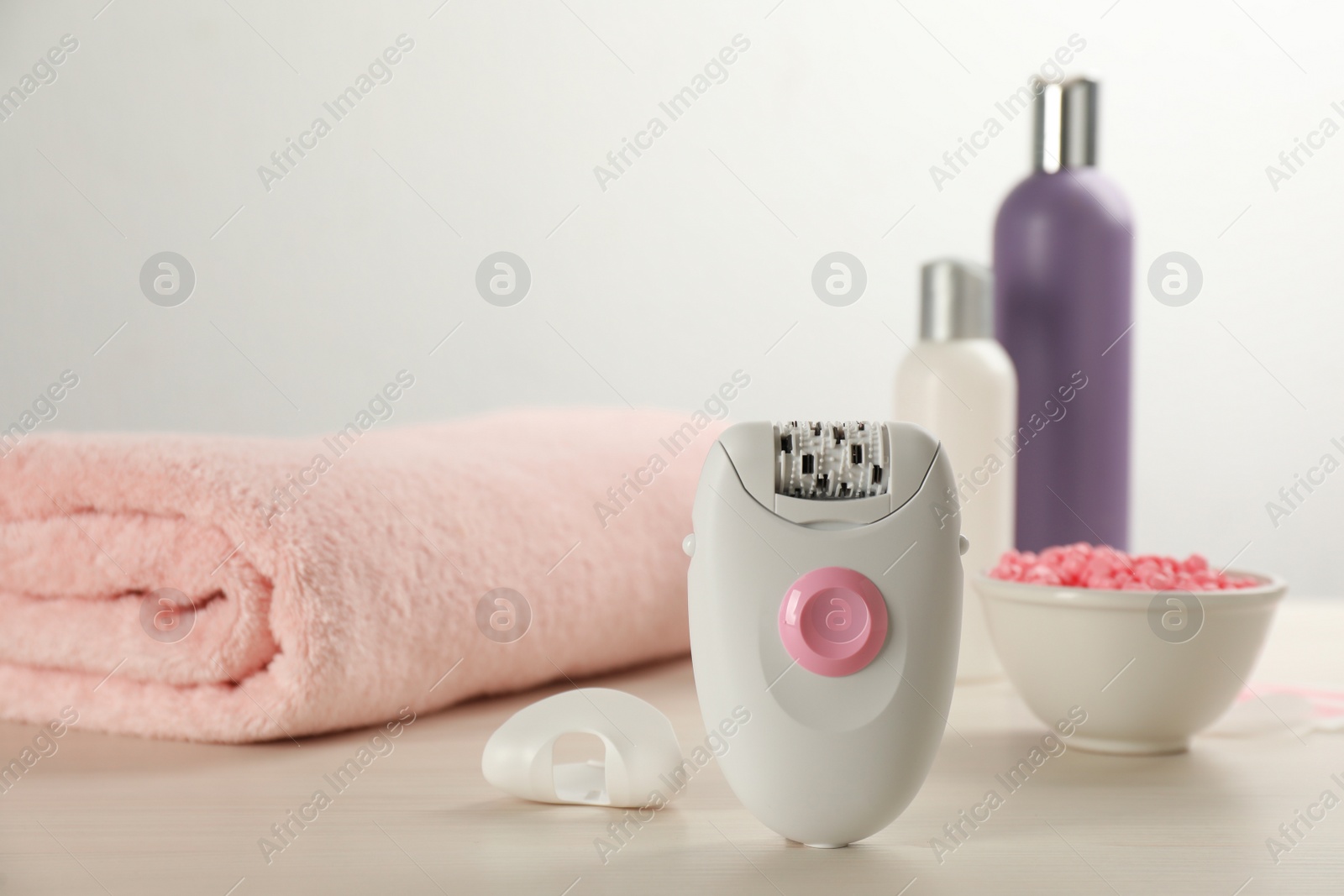 Photo of Modern epilator and other hair removal products on white wooden table