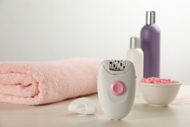 Photo of Modern epilator and other hair removal products on white wooden table