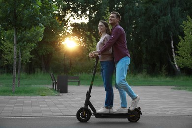 Happy couple riding modern electric kick scooter in park