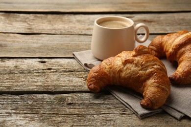 Delicious fresh croissants and cup of coffee on wooden table, space for text