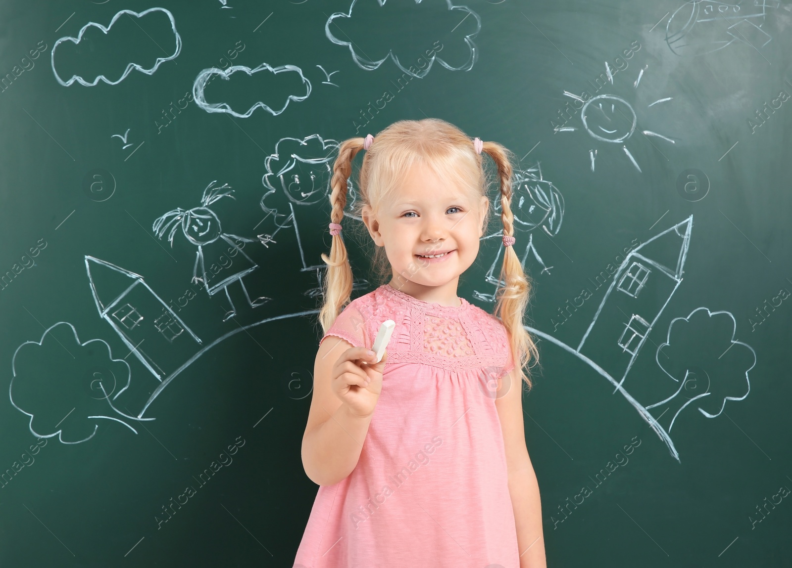 Photo of Little child holding chalk near blackboard with drawing of family