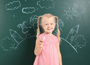 Photo of Little child holding chalk near blackboard with drawing of family