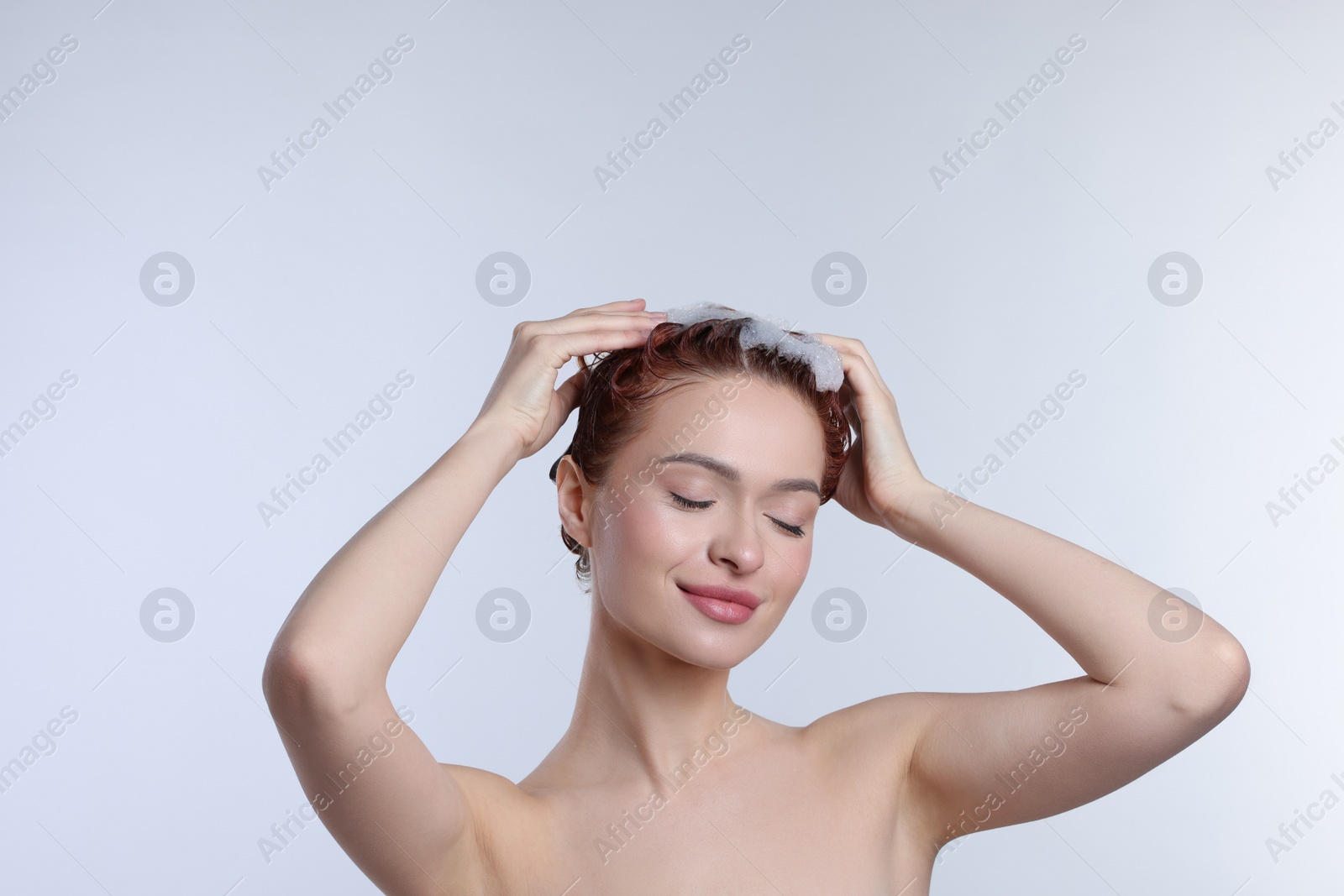 Photo of Happy young woman washing her hair with shampoo on light grey background