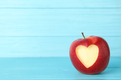 Photo of Red apple with carved heart on table against color background. Space for text