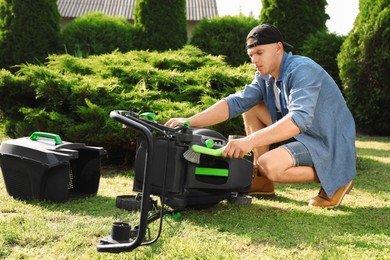 Photo of Young man cleaning lawn mower with brush in garden