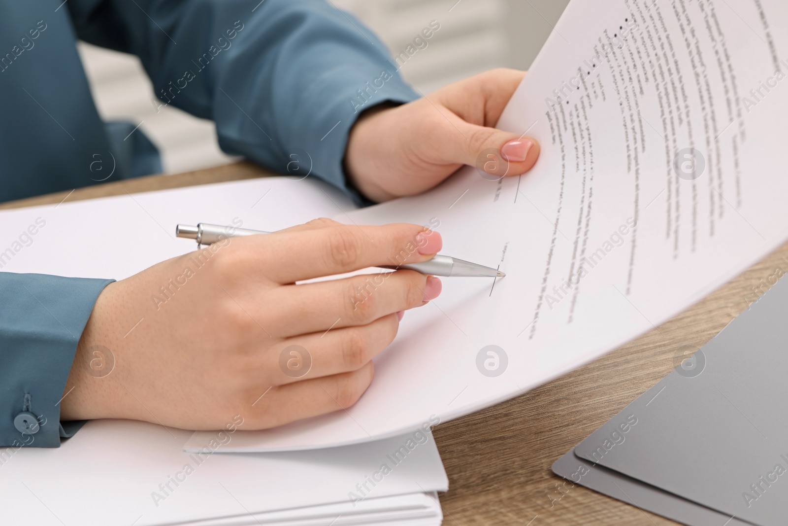 Photo of Woman signing document at wooden table, closeup