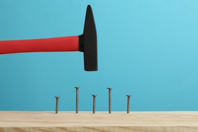 Photo of Hammering nail into wooden surface against light blue background