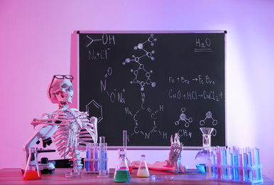 Photo of Skeleton and different chemistry glassware in classroom, toned in pink