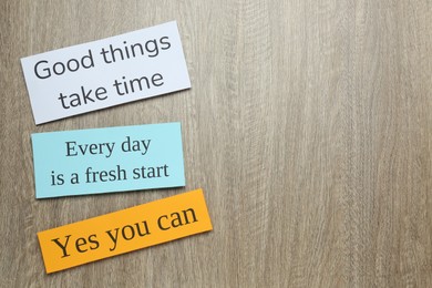 Photo of Notes with motivational quotes on wooden background, flat lay. Space for text