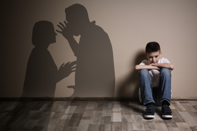 Image of Upset boy sitting on floor and silhouettes of arguing parents 