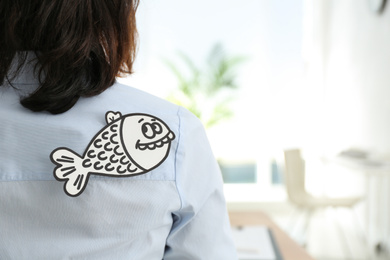 Photo of Woman with paper fish on back indoors, space for text. April fool's day