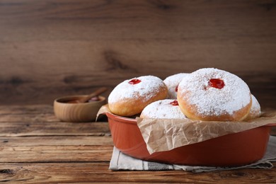 Photo of Delicious donuts with jelly and powdered sugar in baking dish on wooden table. Space for text