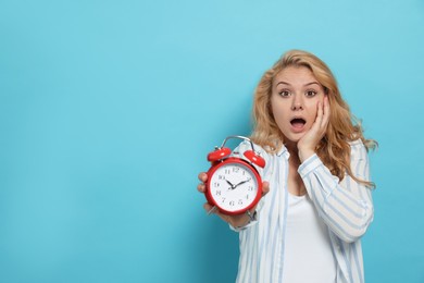 Photo of Emotional woman with alarm clock in turmoil over being late on light blue background. Space for text