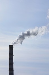 Photo of Polluting air with smoke from industrial chimney outdoors against blue sky. CO2 emissions