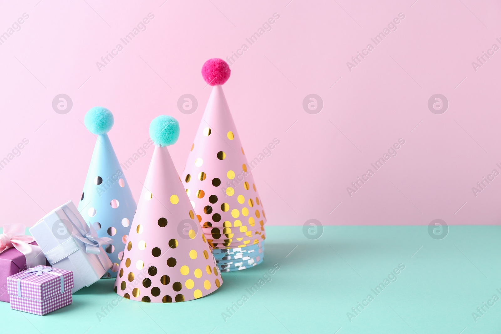 Photo of Party hats and gift boxes on color background, space for text