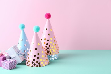 Party hats and gift boxes on color background, space for text