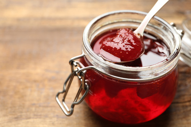 Photo of Delicious pickled strawberry jam in glass jar on wooden table, closeup
