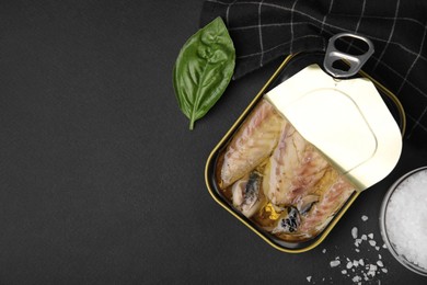 Photo of Open tin can with mackerel fillets and spices on black table, flat lay. Space for text