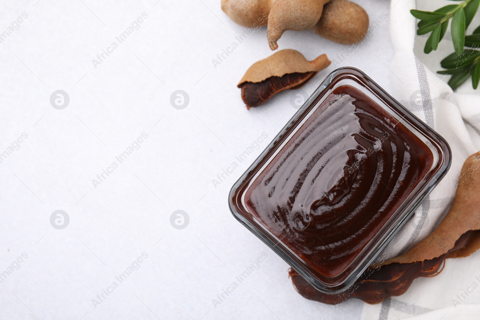 Bowl of tasty tamarind sauce and fresh pods on light table, flat lay. Space for text Photo of Bowl of tasty tamarind sauce and fresh pods on light table, flat lay. Space for text