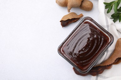 Photo of Bowl of tasty tamarind sauce and fresh pods on light table, flat lay. Space for text