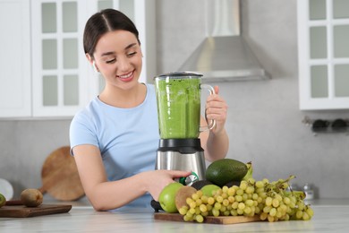 Photo of Beautiful young woman preparing tasty smoothie at white table in kitchen