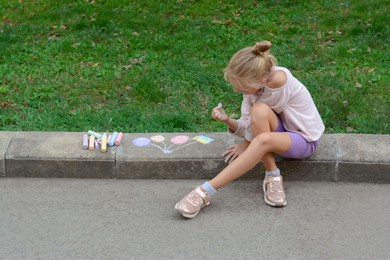 Photo of Little child drawing balloons and ukrainian flag with chalk on curb outdoors, space for text