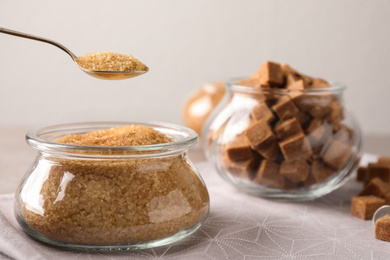 Taking spoon of brown sugar from glass bowl on table