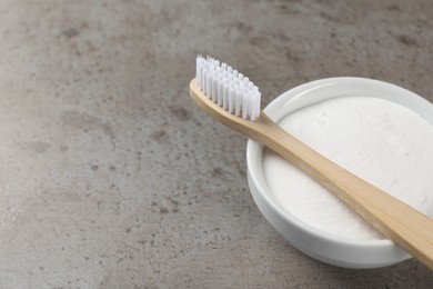 Bamboo toothbrush and bowl of baking soda on grey table, closeup. Space for text