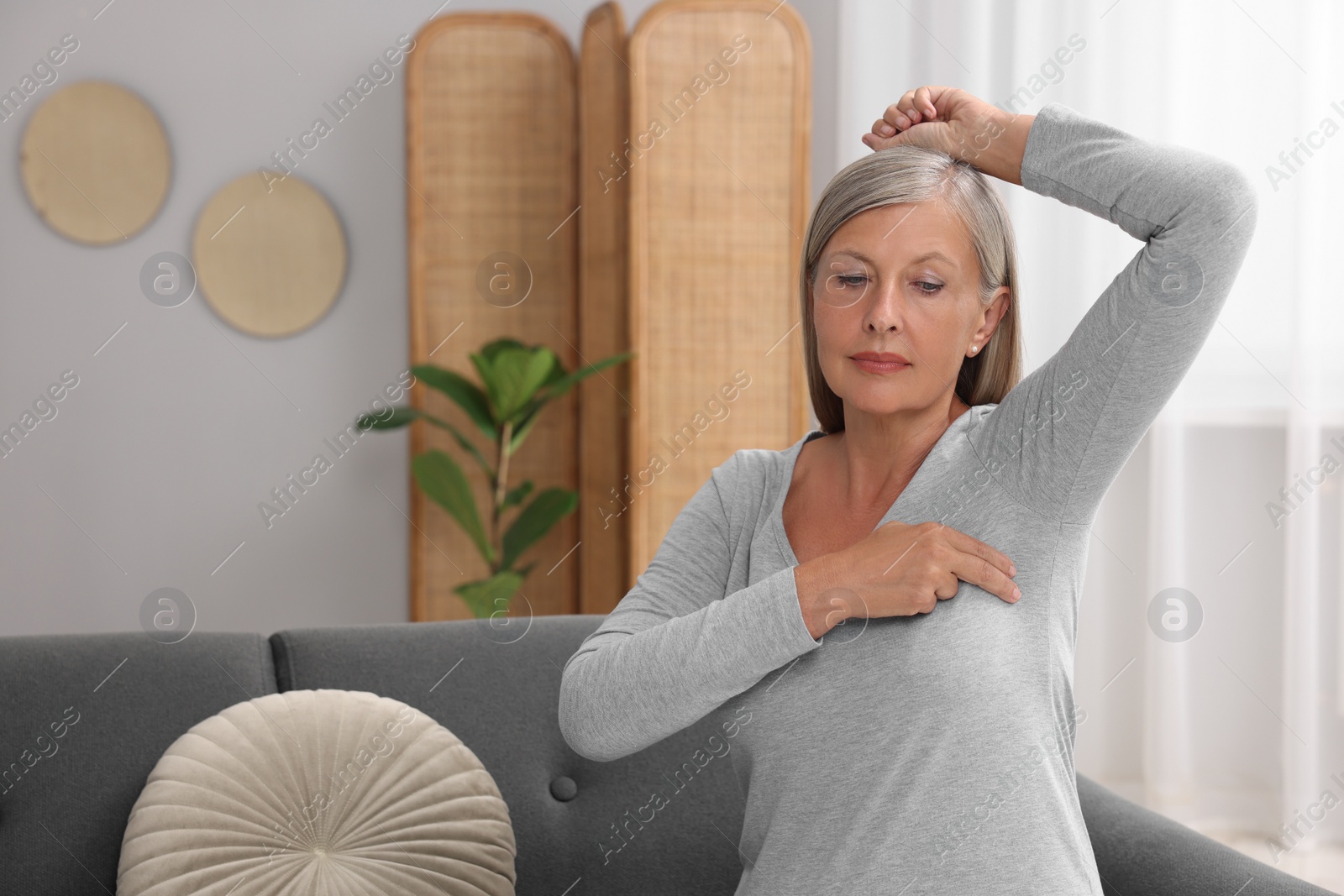 Photo of Beautiful senior woman doing breast self-examination at home, space for text