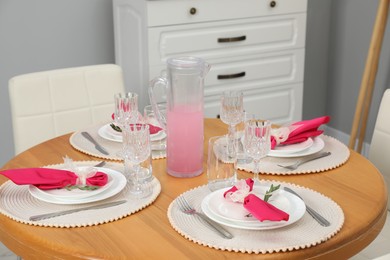 Color accent table setting. Glasses, plates, jug of beverage and pink napkins in dining room